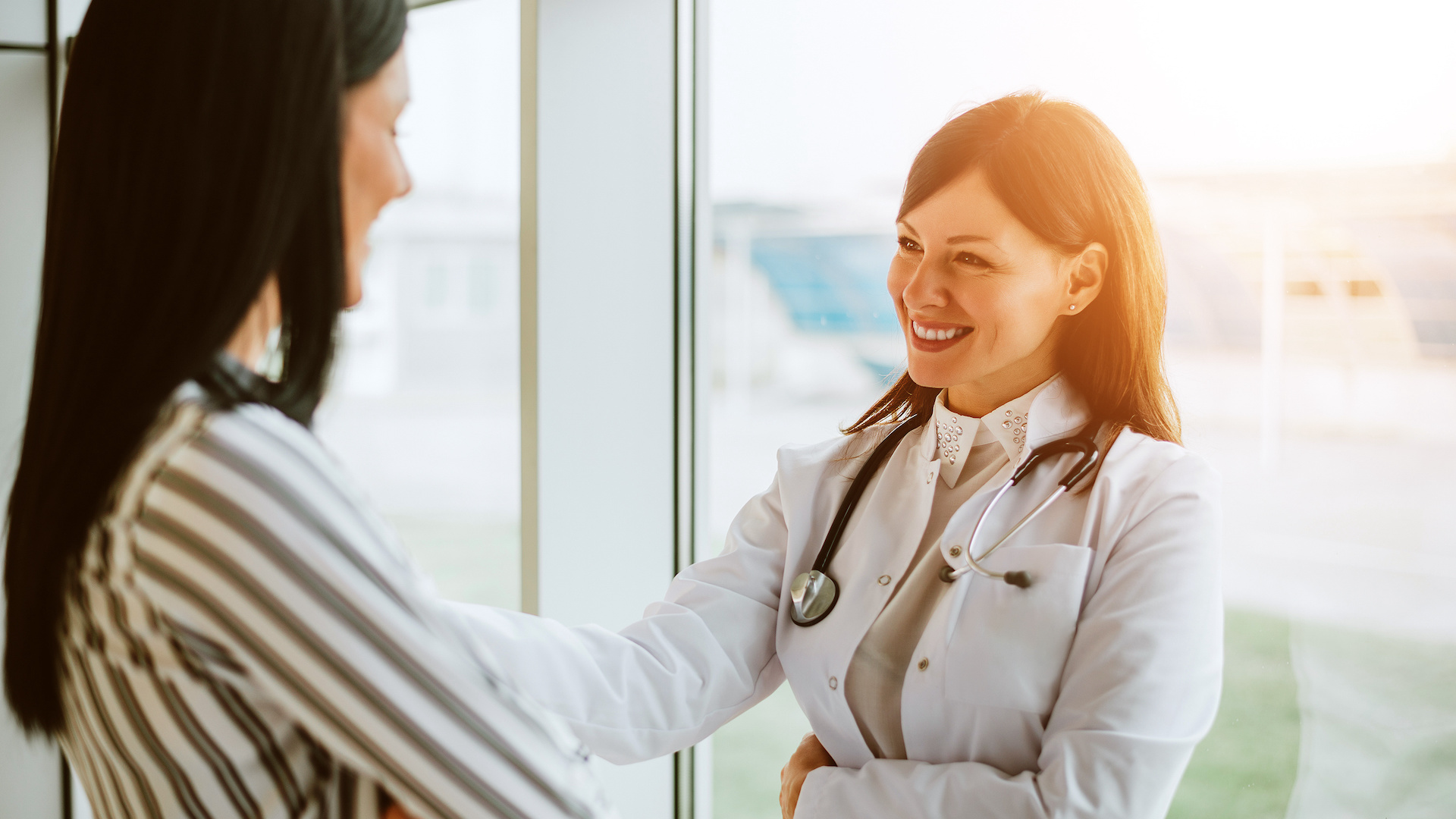 Cheerful woman doctor talking with young woman in office.